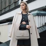 Woman in a beige coat holding a beige handbag in an urban setting
