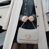Woman holding a beige handbag with a building in the background