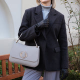 Woman in a dark coat holding a light gray handbag outdoors.