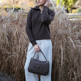 Woman holding a black Carlo Savatelli handbag in front of tall grasses