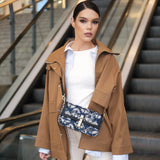 Woman in a brown coat holding a blue floral handbag in an indoor setting.