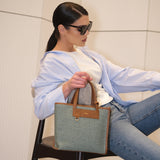 Woman sitting on a chair holding a textured handbag, wearing sunglasses and a light blue shirt.