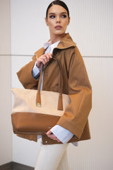 Woman holding a brown and beige handbag against a white wall