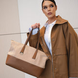 Woman holding a brown and beige handbag wearing a brown coat against a neutral background