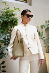 Woman in a white outfit holding a beige handbag with plants in the background