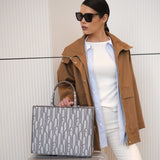 Woman holding a patterned handbag and standing next to a suitcase against a neutral background