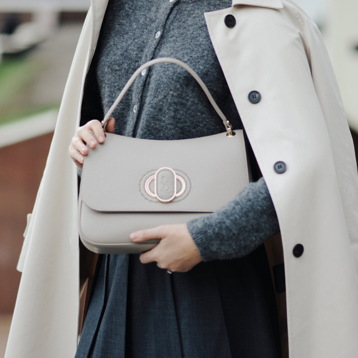 Person holding a beige handbag wearing a beige coat and dark outfit.