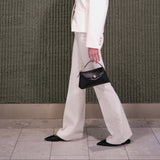 Person wearing a white outfit with a black handbag against a green textured wall.