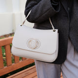 Person holding handbag with a Carlo Salvatelli logo, wearing a dark coat and light pants, outdoors.