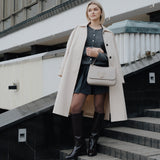 Woman in a beige coat and beige handbag standing on steps with a building in the background