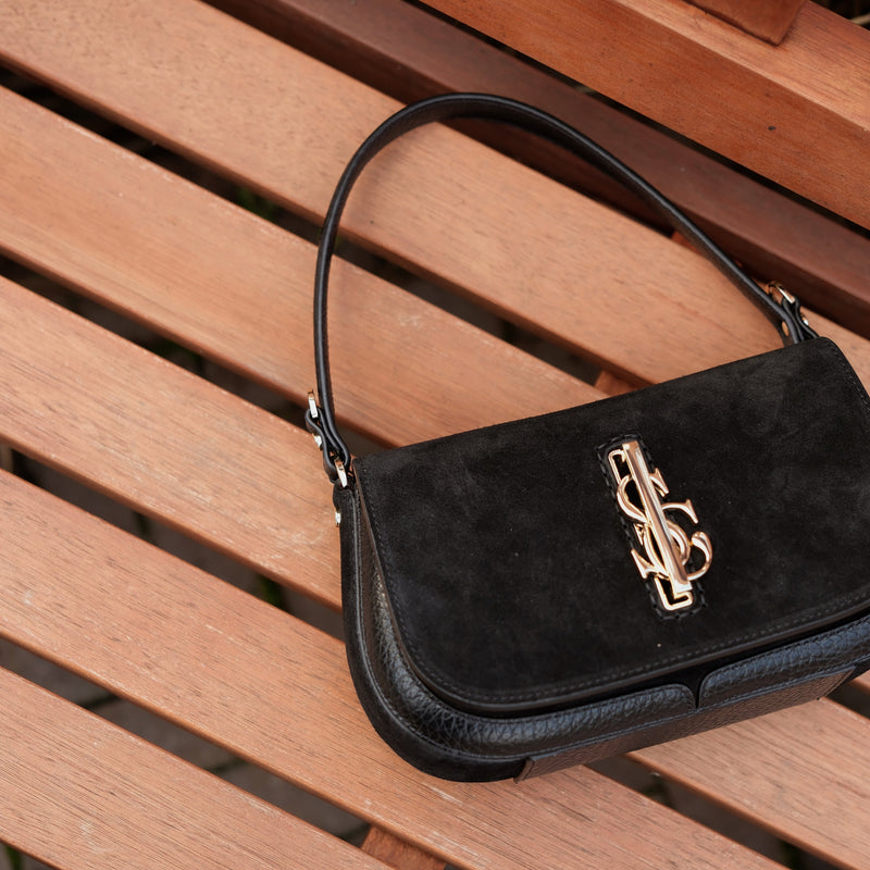 Black handbag with a gold Carlo Salvatelli logo on a wooden surface