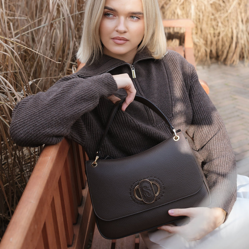 Woman holding a black Carlo Salvatelli handbag outdoors with dry grass in the background