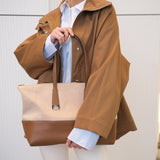 Woman holding a beige and brown handbag wearing a brown coat and white pants.