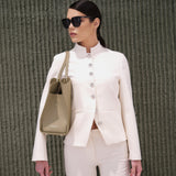 Woman in a white outfit holding a olive handbag against a textured green wall.