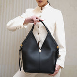 Woman holding a black leather handbag against a neutral background