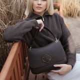 Woman holding a black Carlo Salvatelli handbag outdoors with dry grass in the background