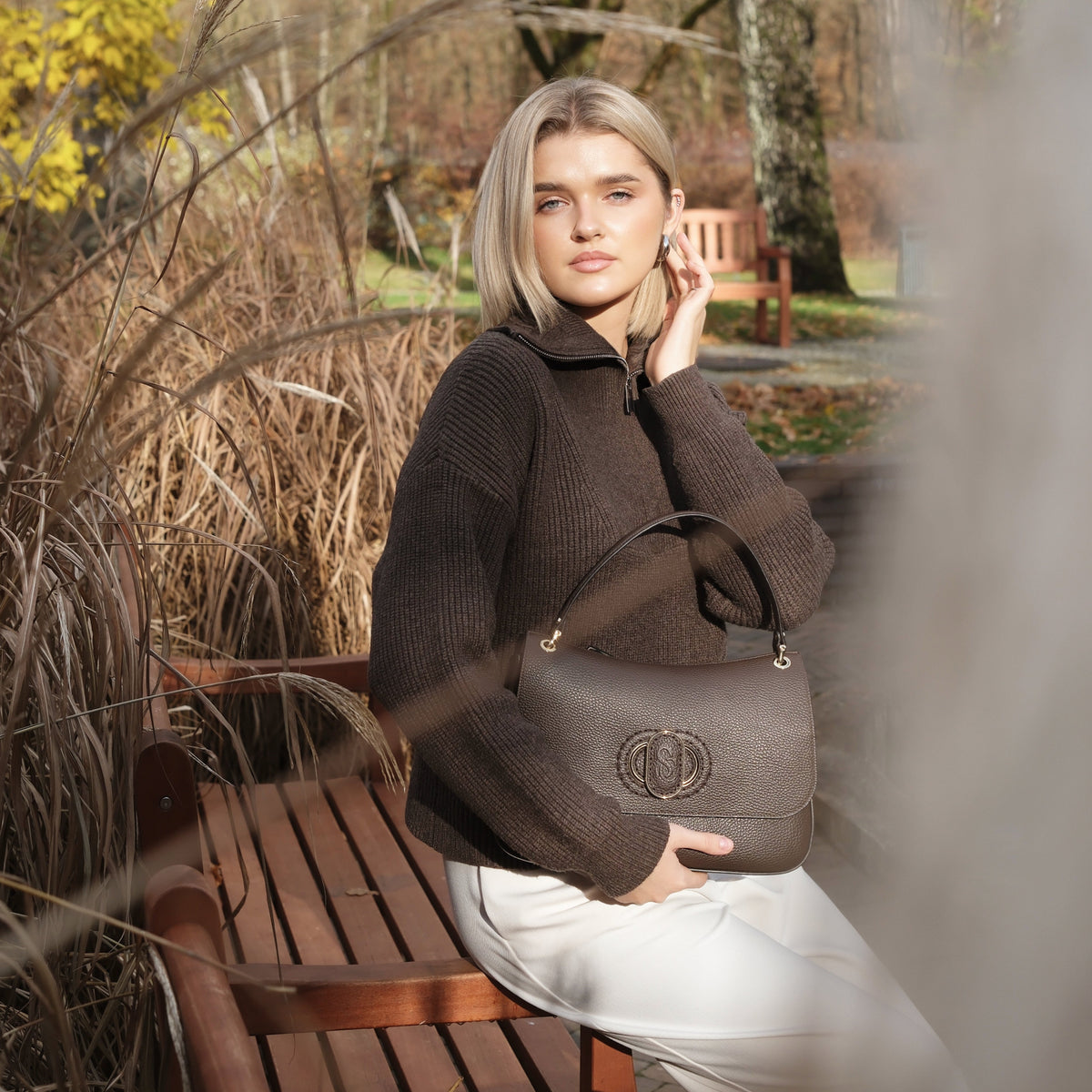 Woman holding a Carlo Salvatelli handbag in an autumnal park setting
