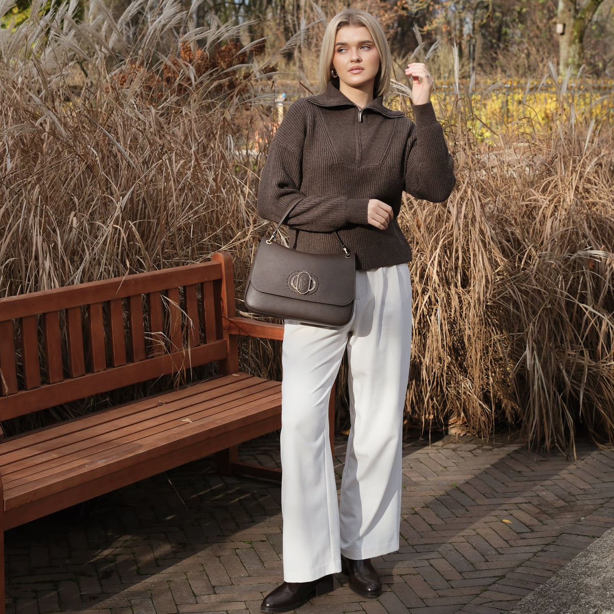 Woman standing in a park with dry grass and a bench in the background