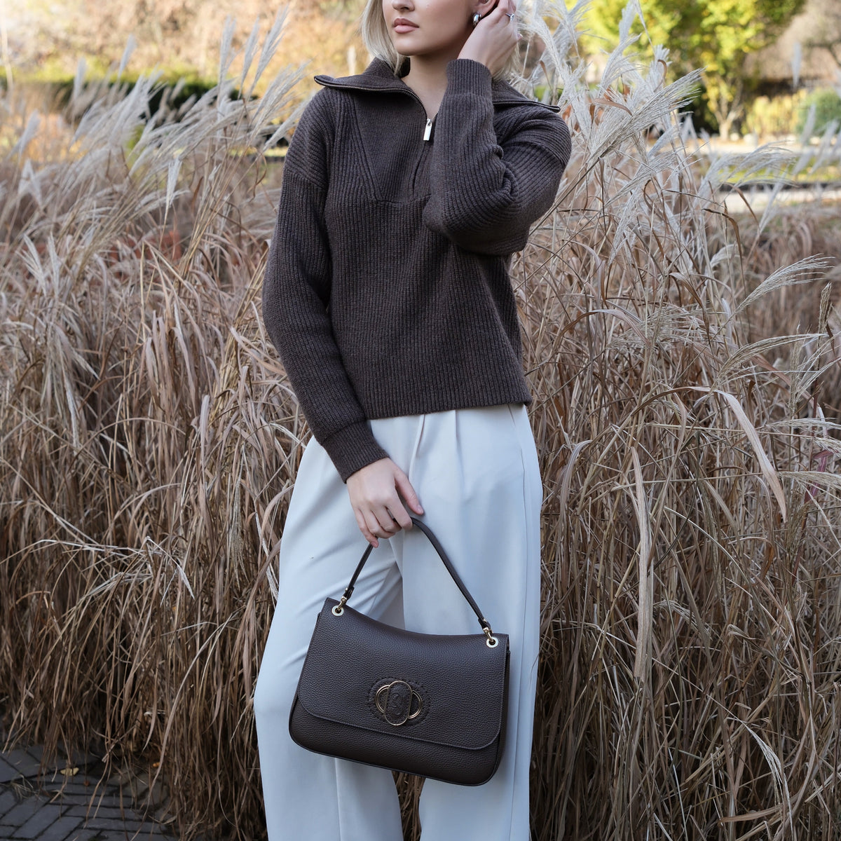 Woman holding a black Carlo Savatelli handbag in front of tall grasses