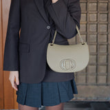 Woman wearing a black blazer and blue skirt with a light green handbag against a textured wall.