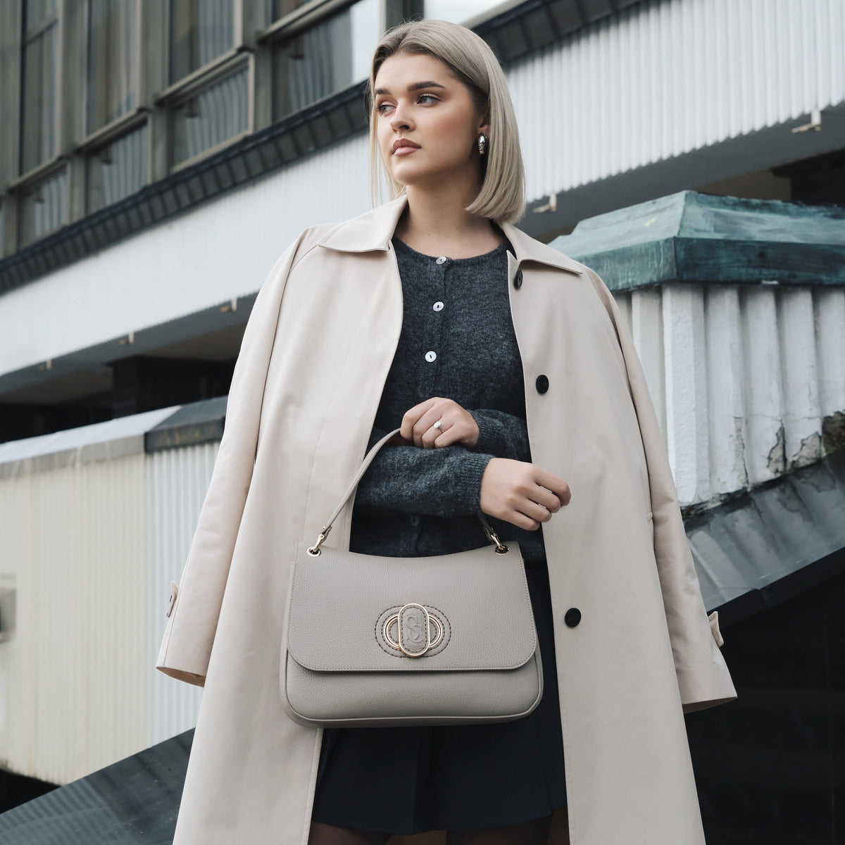 Woman in a beige coat holding a beige handbag in an urban setting